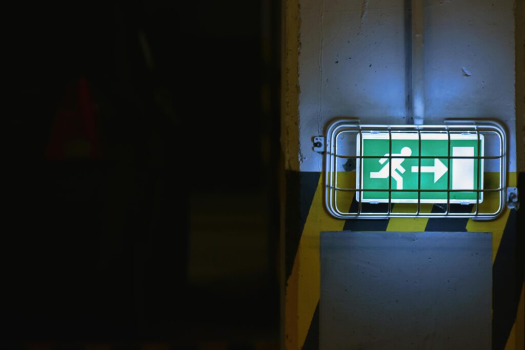 Uhistule Green emergency exit sign with arrow in dimly lit area, emphasizing safety.