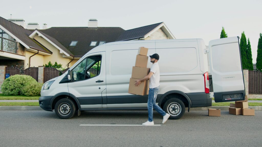 Uhistule Man unloading cardboard boxes from a delivery van in a suburban neighborhood street.