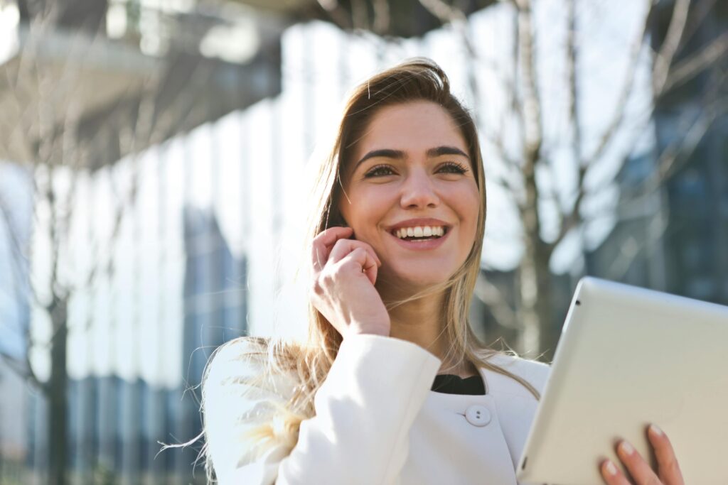 Uhistule Confident businesswoman using her tablet and phone, smiling outdoors in sunlight.